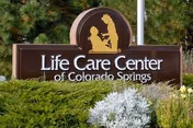 Outdoor sign for Life Care Center of Colorado Springs surrounded by green bushes and plants.