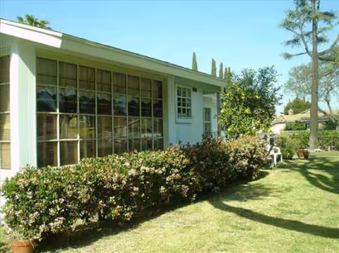 Exterior view of a single-story senior care facility with large windows and shrubs.