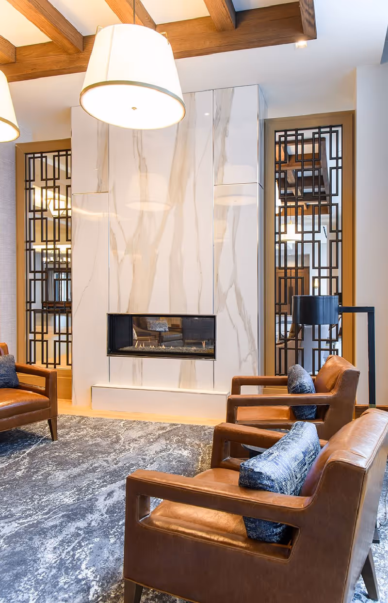 Modern lounge with leather armchairs arranged around a built-in marble fireplace under pendant lights.