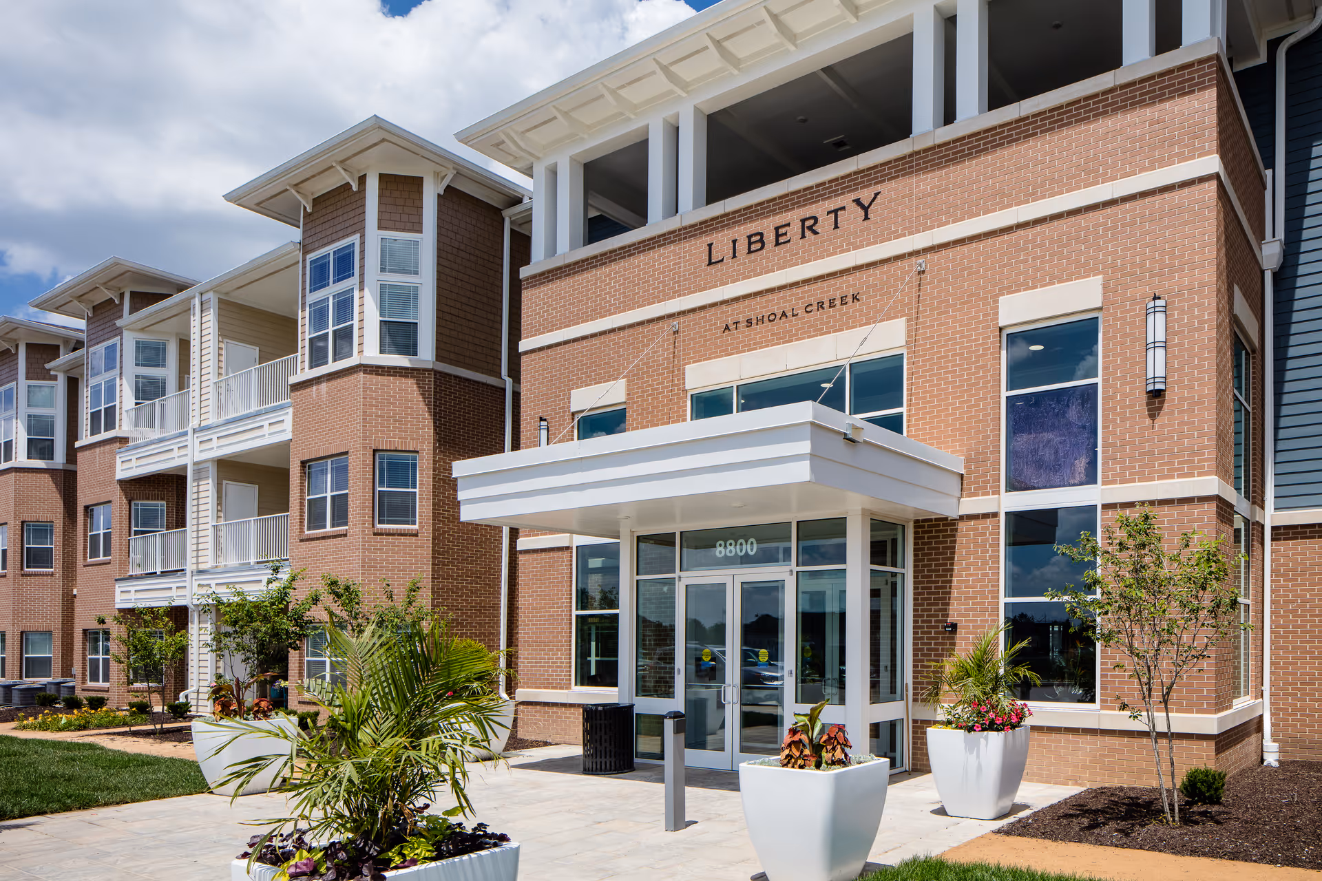 Front entrance of the Liberty at Shoal Creek building with a brick facade, glass doors, balconies, and planters.