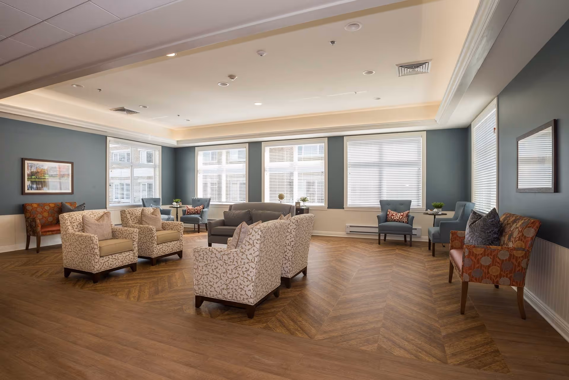 Bright lounge/common room with multiple armchairs, sofas, side tables and large windows in a retirement community.