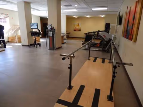 Indoor rehabilitation gym in a senior living facility with parallel bars and exercise equipment.