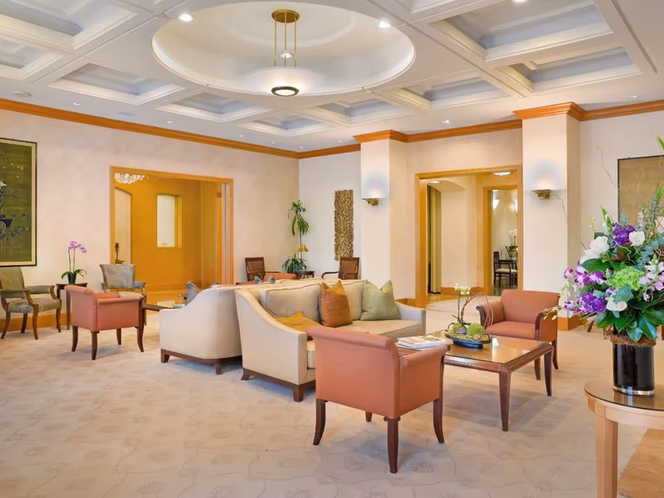 Spacious, well-lit lounge with sofas, armchairs, a coffee table, and a large floral arrangement beneath a coffered ceiling.
