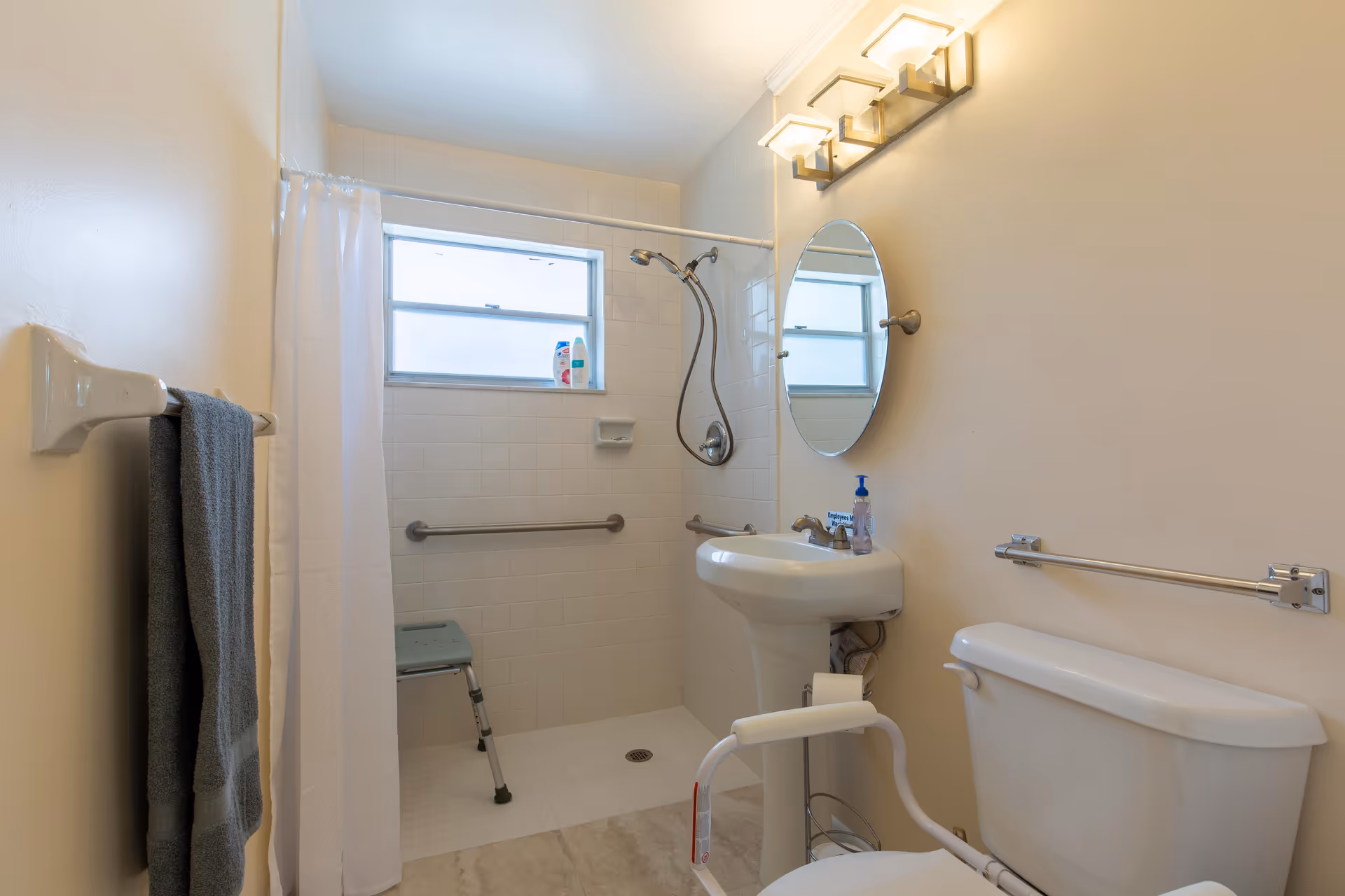 Accessible bathroom with a walk-in shower, grab bars, pedestal sink, and a toilet with safety rails.