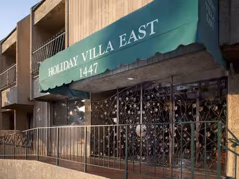 Exterior view of a building entrance with a green awning reading 'Holiday Villa East'.