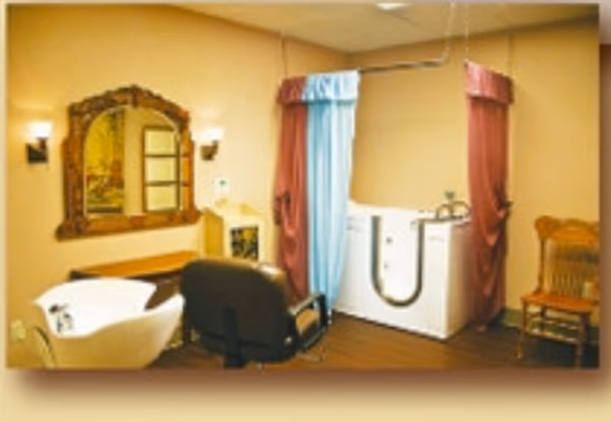 Interior room with a hair washing station including a white basin and black chair, a large ornate mirror on the wall, a wooden chair, and a bathing tub with curtains for privacy.