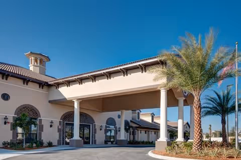 Exterior of Palm Bay Memory Care facility with arches, columns, and palm trees under blue sky.