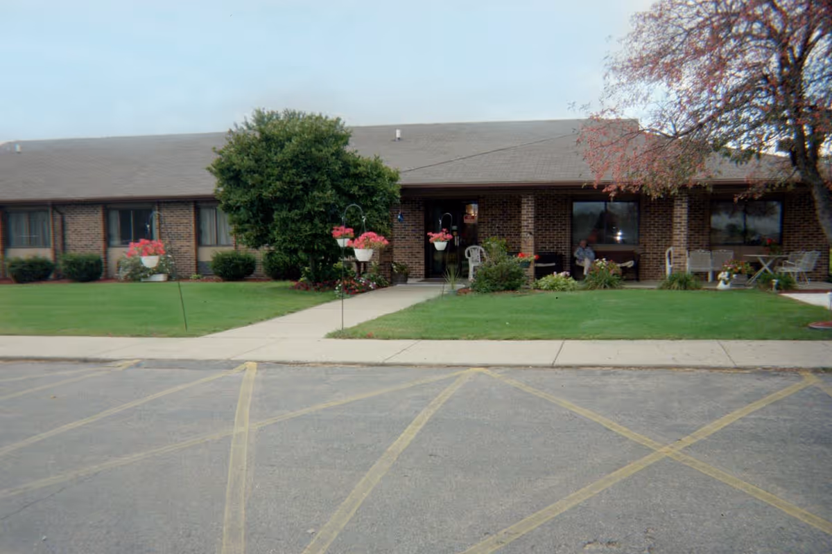 Single-story brick building front with a lawn, walkway, hanging flower baskets and a parking area.