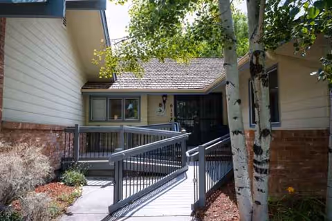 Exterior view of a senior living facility entrance with a ramp and surrounding greenery