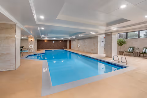 Indoor community swimming pool with lounge chairs, potted plants, and lifebuoys.