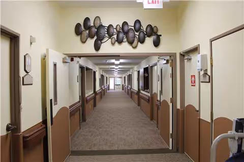 Long, well-lit hallway in a senior living facility with multiple doors along both walls.