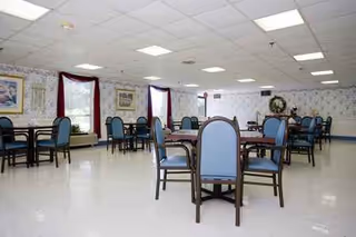 Spacious senior living facility dining room with blue upholstered chairs around dark wooden tables.