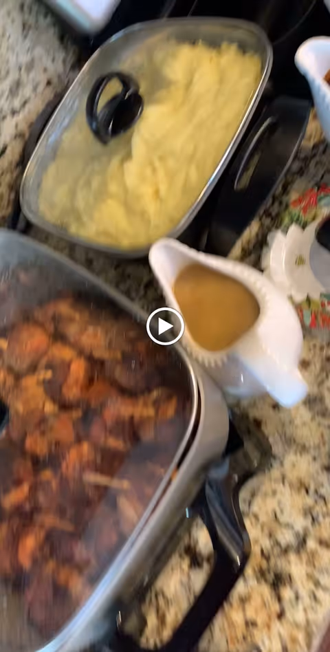 Covered pans of mashed potatoes and roasted meat with a gravy boat of gravy on a granite countertop.