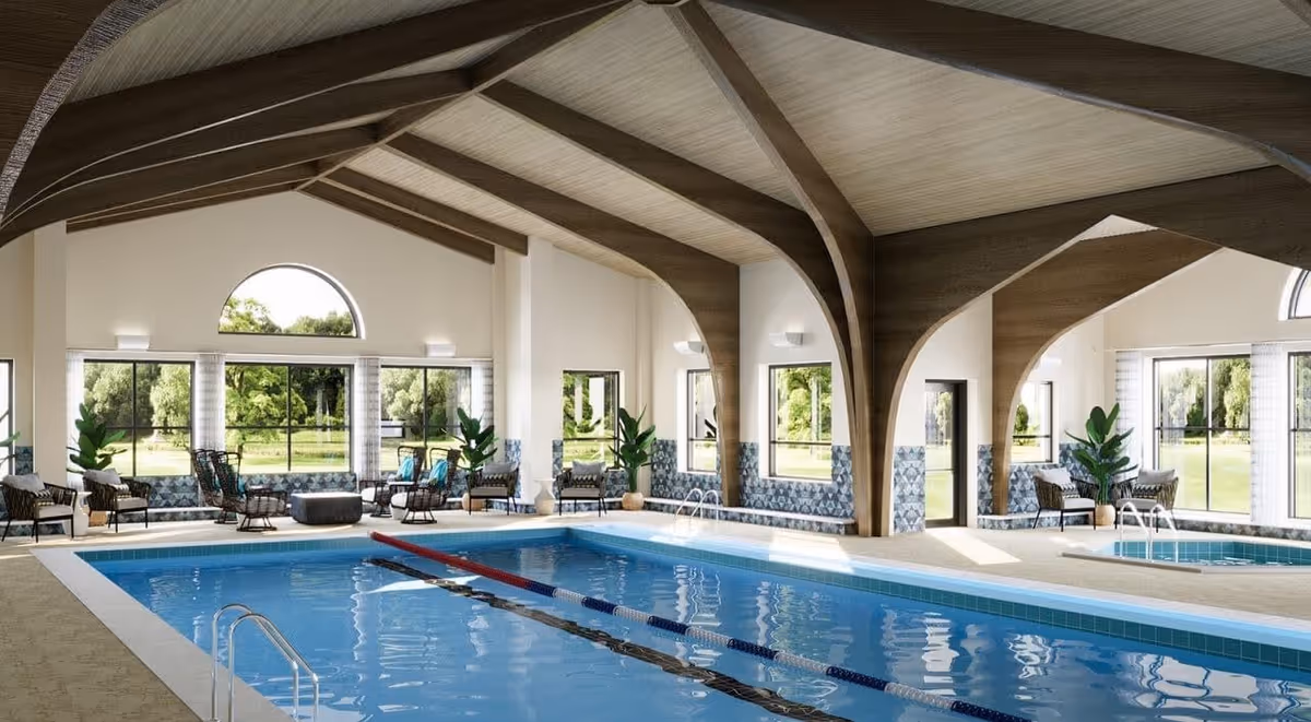 Indoor swimming pool area with a lap pool and a smaller hot tub or spa pool. The room features large windows with views of greenery outside, wooden beams on the ceiling, and several seating areas with chairs and plants around the pool.
