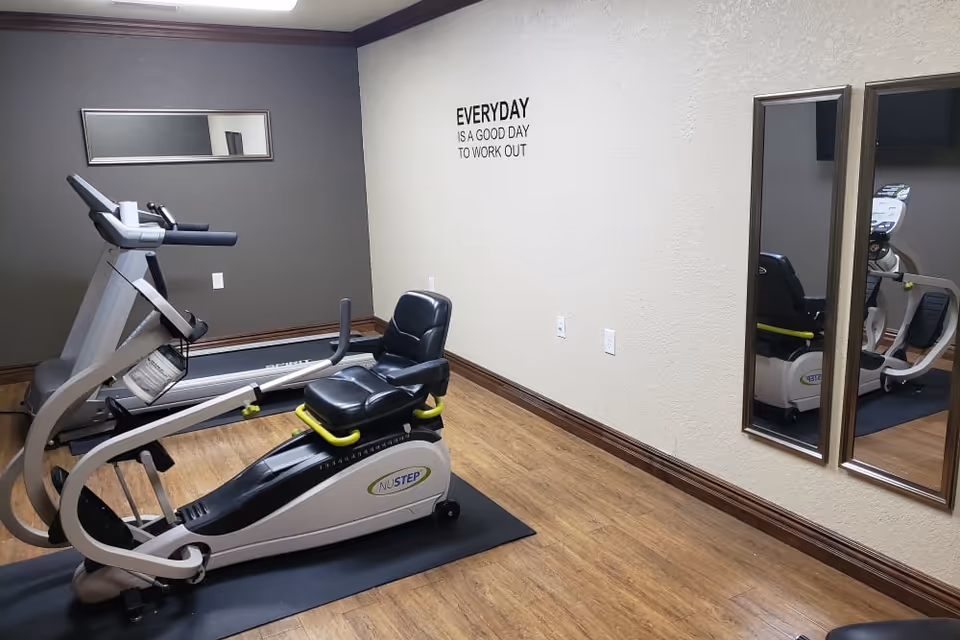 Small exercise room with a recumbent stepper and treadmill, mirrors, and a wall decal reading "EVERYDAY IS A GOOD DAY TO WORK OUT".