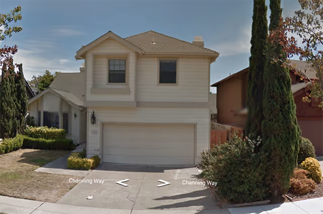 Two story beige suburban house with a double garage on a residential street.