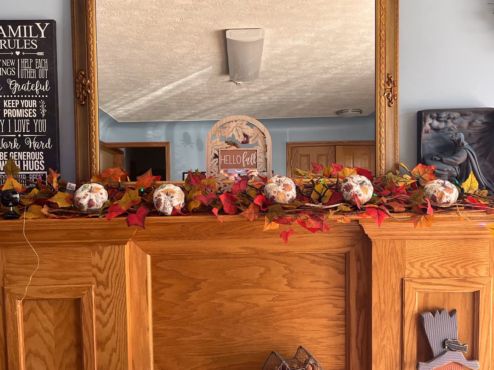 Wooden fireplace mantel decorated with autumn garland and decorative pumpkins beneath a large framed mirror.