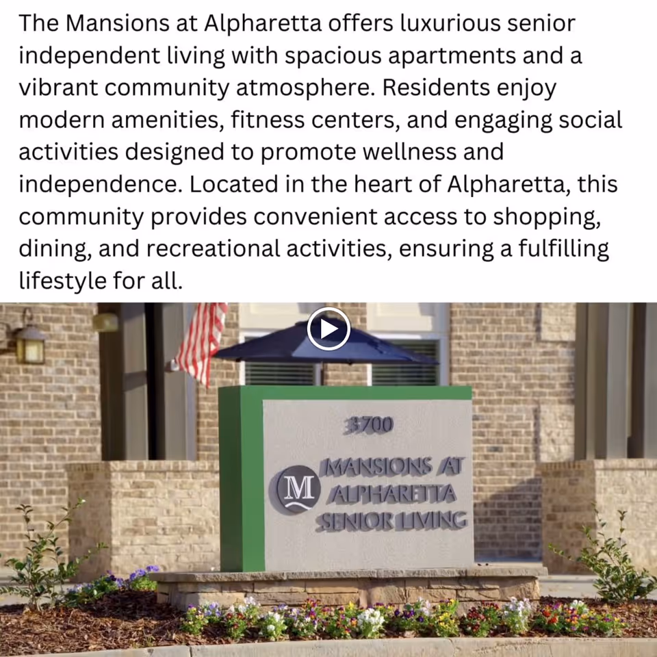 Outdoor view of a stone sign for Mansions at Alpharetta Senior Living, surrounded by flowers and landscaping, with a brick building and an American flag in the background.