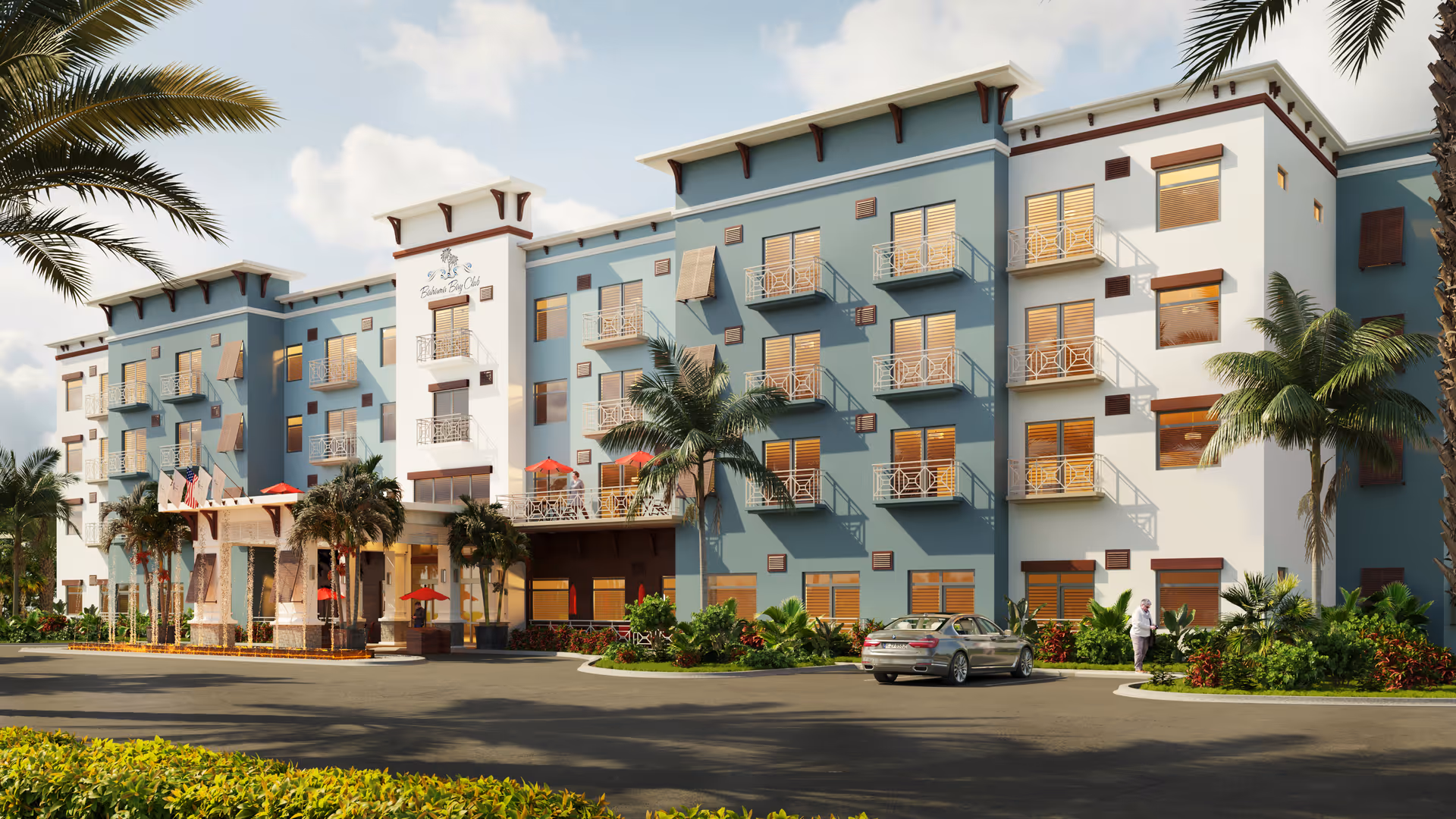 Exterior view of a modern senior living facility named Bahama Bay Club Luxury Senior Living, featuring a multi-story building with balconies, palm trees, landscaped greenery, a parked car, and a person walking near the entrance under a partly cloudy sky.