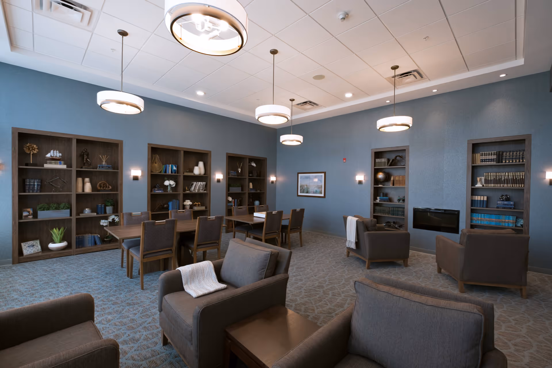 Communal lounge with armchairs, dining tables, built-in bookshelves and pendant lighting.