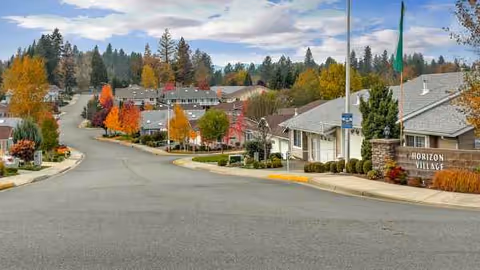 Autumn trees line a paved street toward Horizon Village's building front entrance.