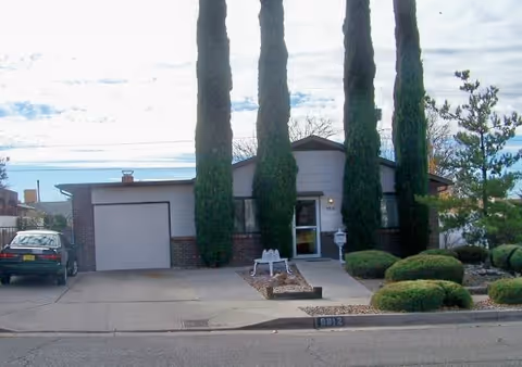 Front view of a single-story senior home with a driveway, garage, and tall trees.