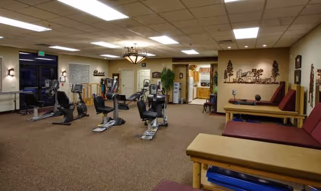 A spacious indoor fitness room with several recumbent exercise bikes, weight benches, padded lounge benches, and wall decorations.