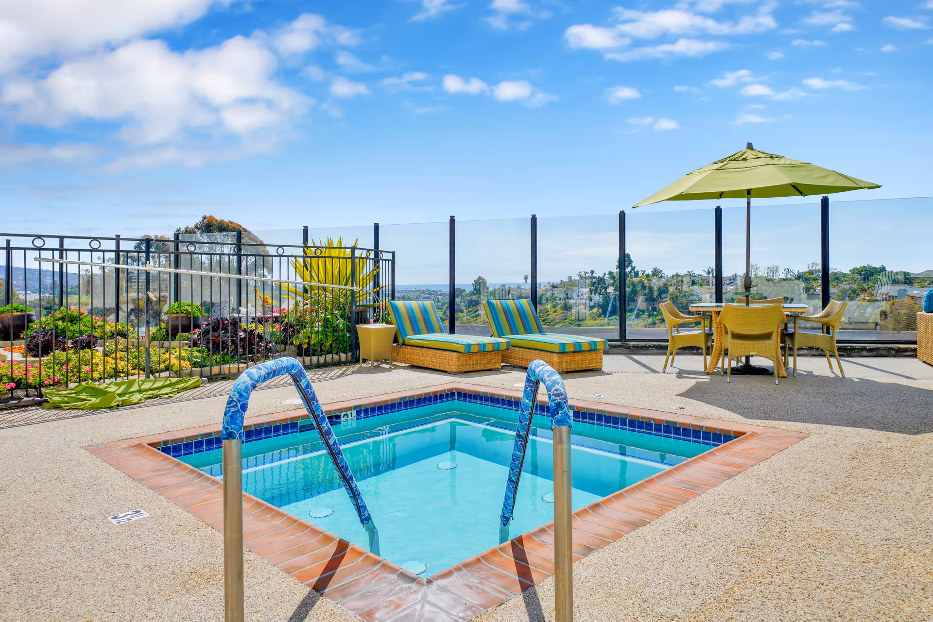 Rooftop patio with a small square pool or hot tub, striped lounge chairs, a table with a green umbrella, and a scenic view.