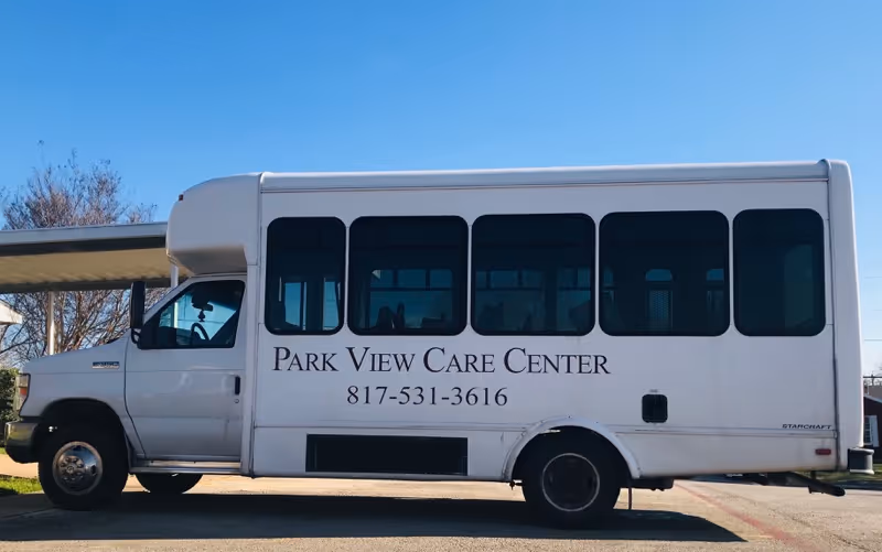 A white shuttle bus parked outside under a clear blue sky. The side of the bus displays the text 'Park View Care Center' and a phone number '817-531-3616'.