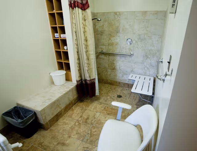 Tiled accessible bathroom with a walk-in shower, fold-down bench, grab bar, shower curtain, seating and cubby shelving.