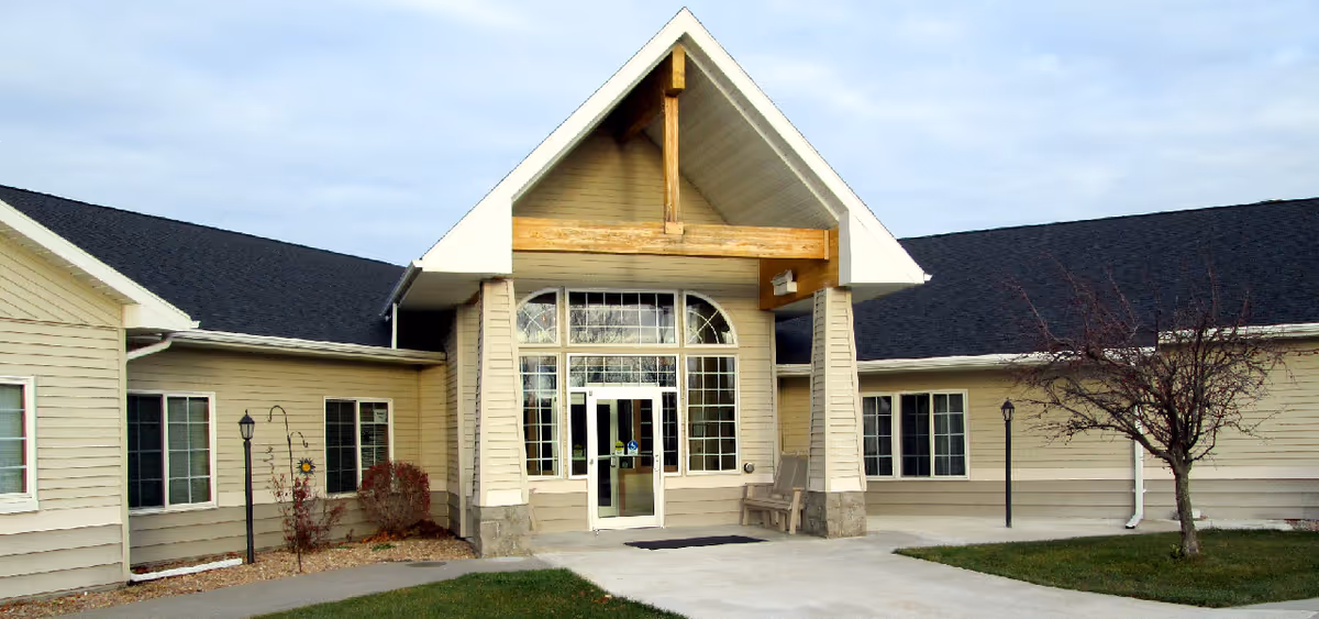 Front entrance of a beige single-story building with a covered gabled portico and glass double doors.