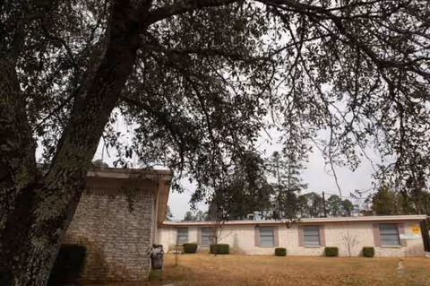 Exterior view of a single-story senior living facility with a large tree in foreground.