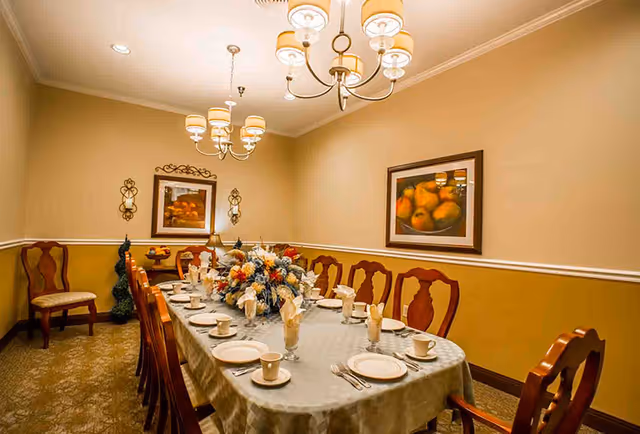 A formal dining room with a long table set with plates, cups, napkins and a central floral arrangement under chandeliers.