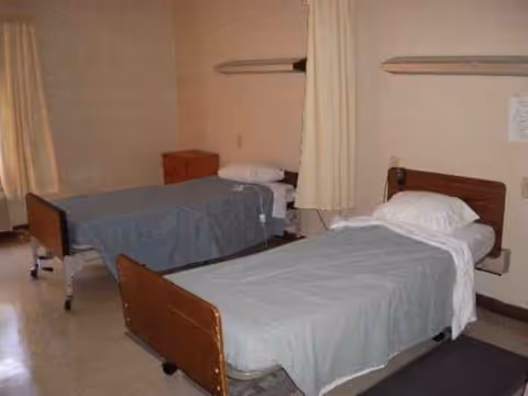 Two single beds with blue sheets in a shared bedroom separated by curtains.