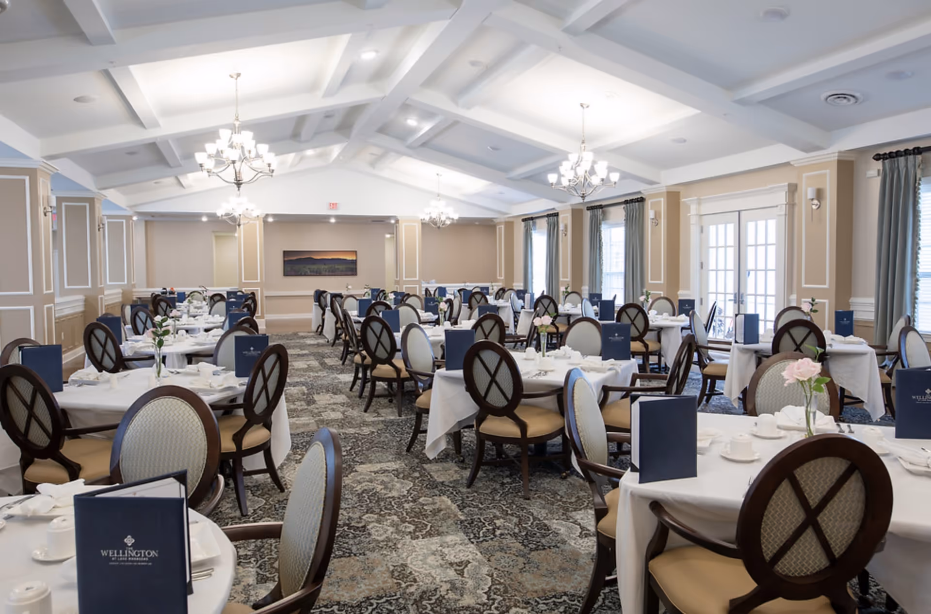 Spacious formal dining room with round tables set for service, chandeliers, and upholstered chairs.