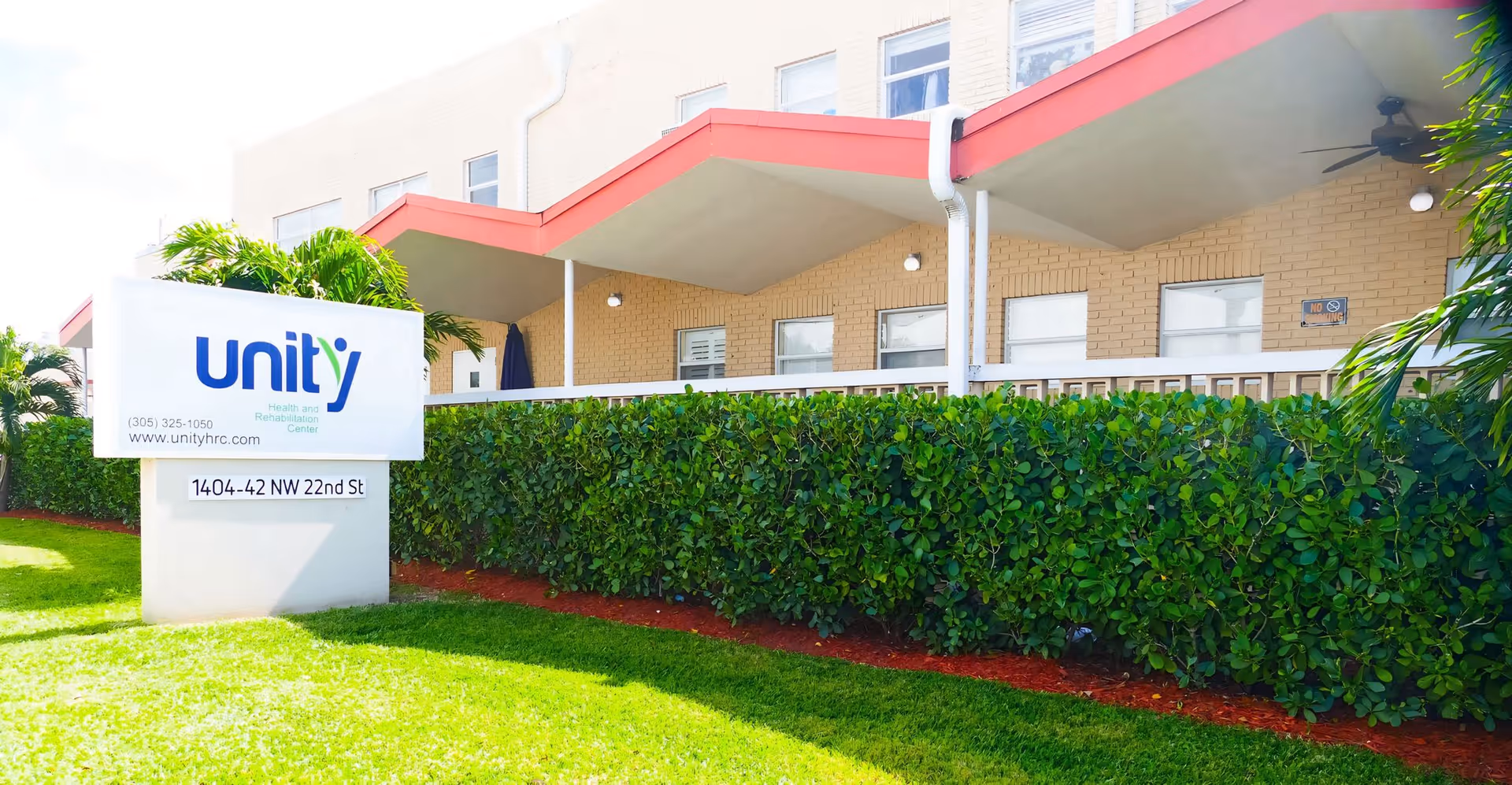 Front exterior of Unity Health and Rehabilitation Center showing the building facade, a manicured hedge and lawn, and a freestanding sign with the 'unity' logo and address.