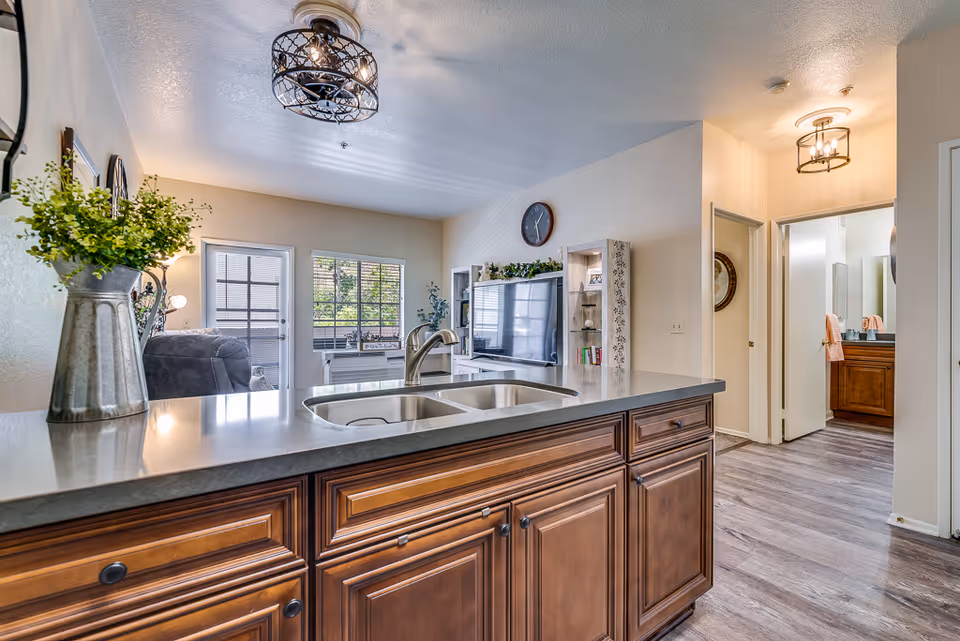 Open-plan kitchen with a large island and double sink looking into a bright living room and hallway.
