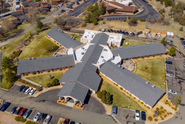 Aerial view of a star-shaped single-story health facility with four long wings, surrounding lawns, and parked cars.