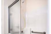 A clean and simple shower area with a frosted glass sliding door, a white showerhead, and a horizontal grab bar mounted on the wall for safety.