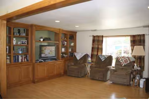 Cozy living room with wooden built-in shelving, TV, recliners, and a window with curtains.