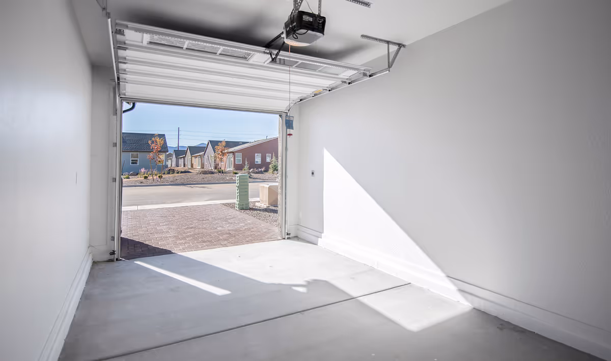 Interior view of an empty single-car garage with the door open to a suburban street and houses.