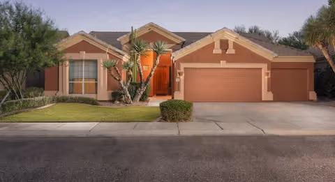 Single-story stucco house with a three-car garage, landscaped front yard, and palm trees at dusk.
