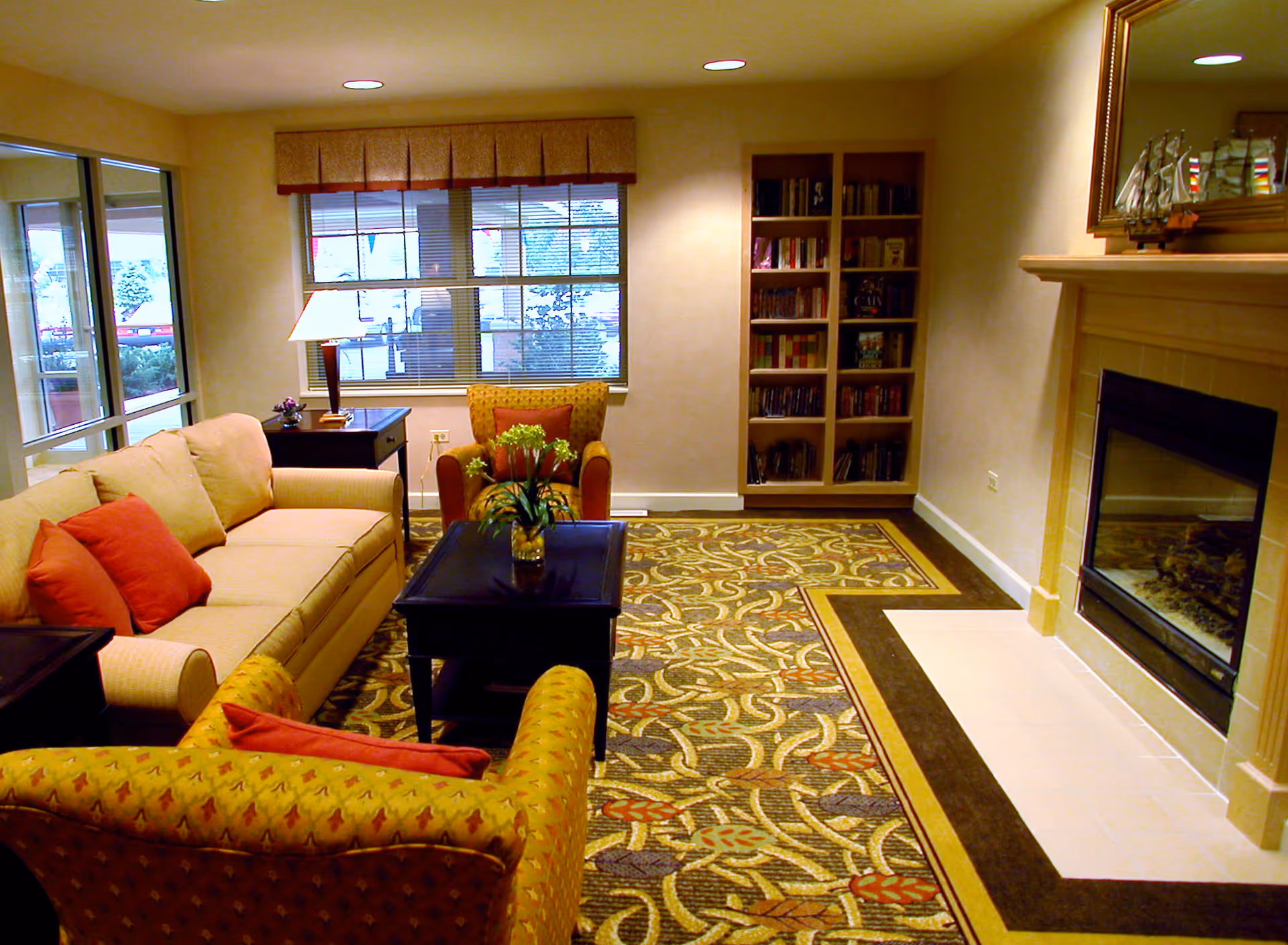Cozy seating area with sofa, armchairs, coffee table, bookshelf, and fireplace in a lounge.