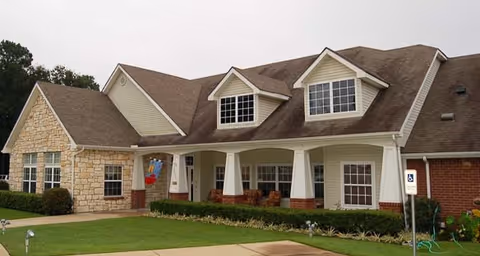 Front exterior of a residential-style building with a covered porch, dormer windows, and landscaped lawn.