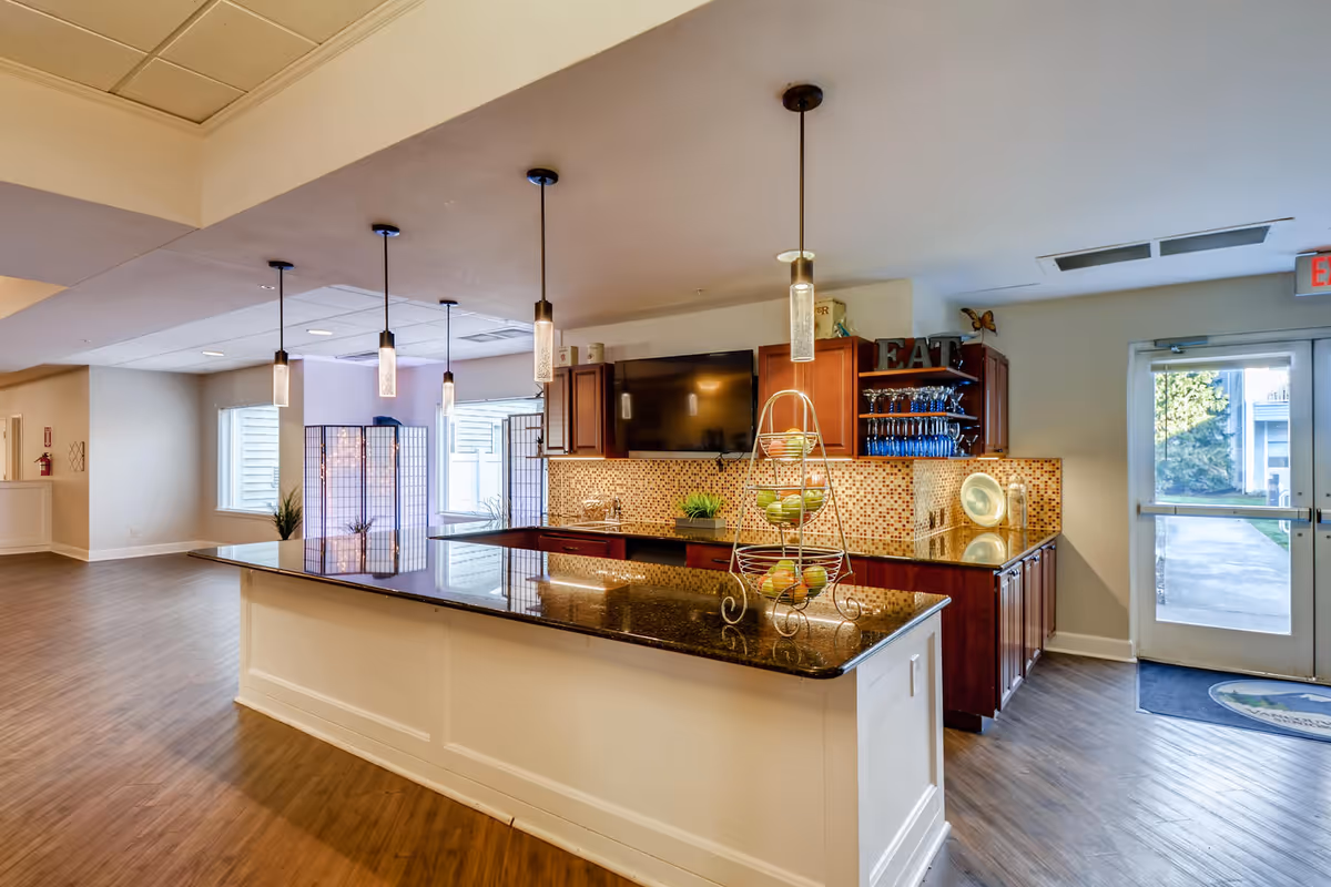 Open communal kitchen area with a large island, pendant lights, mosaic tile backsplash and wood cabinets.