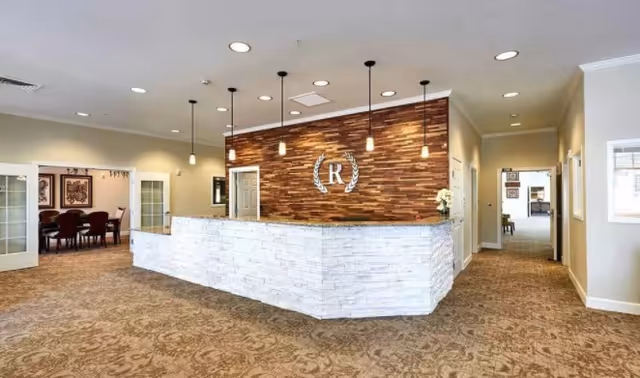 Reception lobby with a stone-faced front desk, wood accent wall featuring an 'R' logo, pendant lights, and carpeted floors.