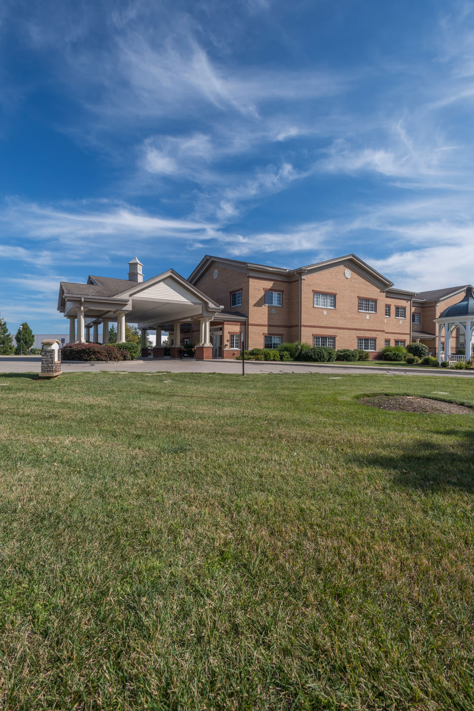 A brick senior living facility surrounded by green grass and under a blue sky.