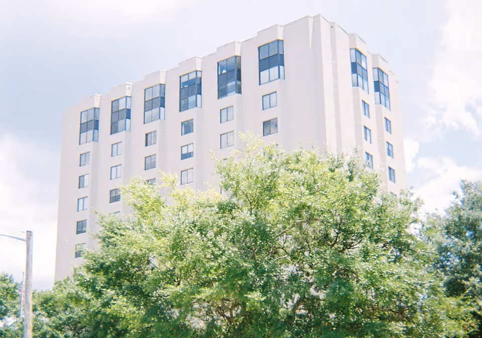 A tall senior living facility building surrounded by trees.