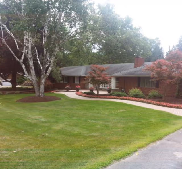 Single-story brick building with a curved paved walkway, manicured lawn and trees in the front yard.