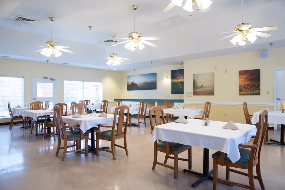 Bright dining room with tables set for meals, wooden chairs, and ceiling fans.